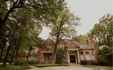 Large brick house surrounded by tall trees.