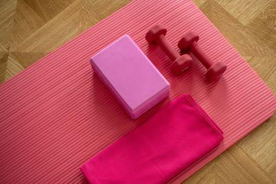 Pink yoga mat with dumbbells, block, and towel on wooden floor.