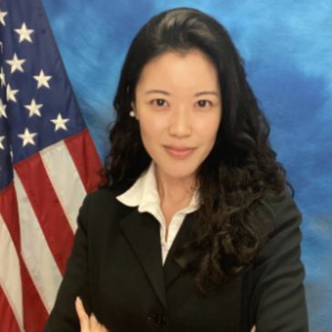 Professional woman posing with American flag in background.