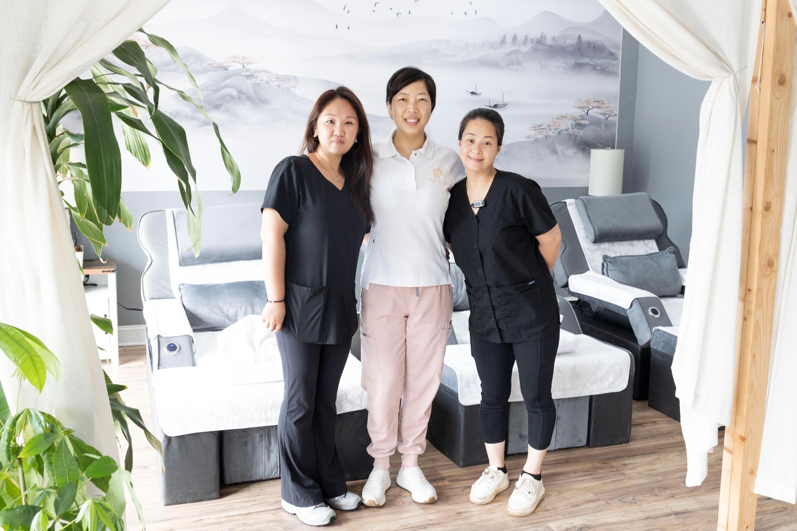 Three women standing together in a spa-like setting, smiling.