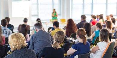 a woman in a green dress presenting to a large audience at a business conference