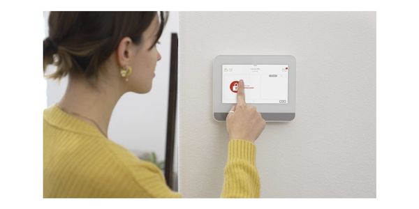 Woman using home security system on wall panel.