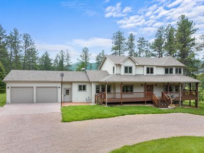 Two-story house with a large porch and a double garage surrounded by trees.