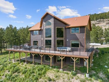 Modern two-story house with large windows and wraparound deck in a forested area.