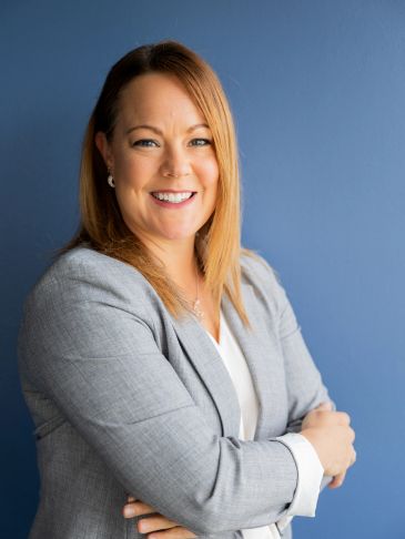 Confident woman in a grey blazer smiling against a blue background.
