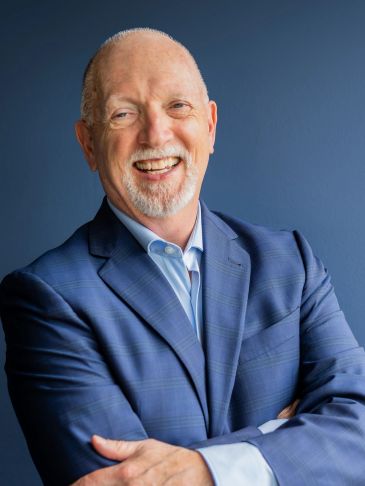Smiling man in a blue suit standing against a blue background.