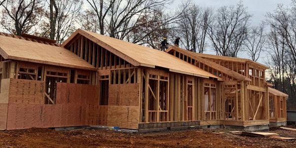 Wooden frame of a house under construction with workers on the roof.
