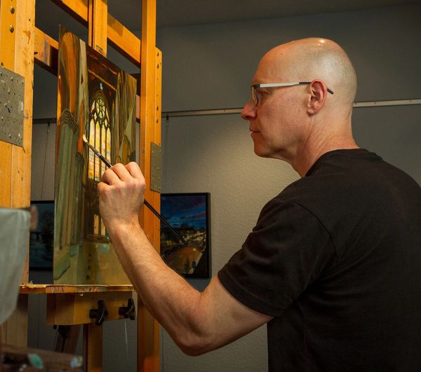 A man painting a cathedral window on a canvas indoors.