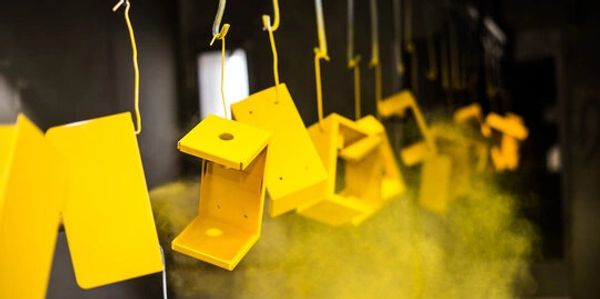 Yellow metal parts hanging and being spray painted.