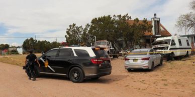 Police vehicles and an officer at a rural property with several vehicles parked.