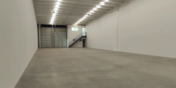 Interior de un almacén vacío con paredes blancas y techo alto.
