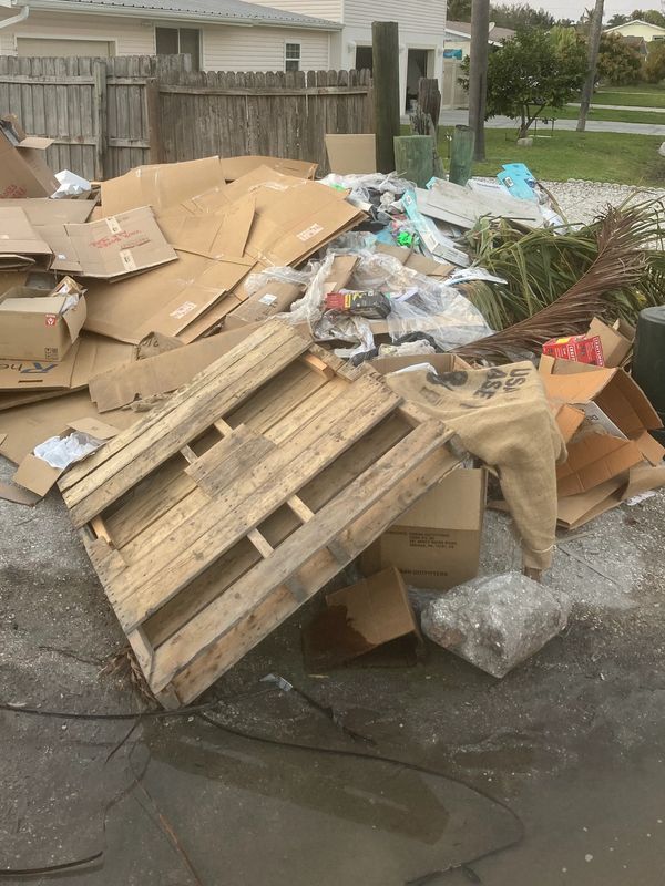 Pile of discarded cardboard, wooden pallet, and various trash outdoors.
