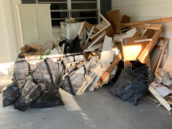 A pile of construction debris and black garbage bags in a garage.