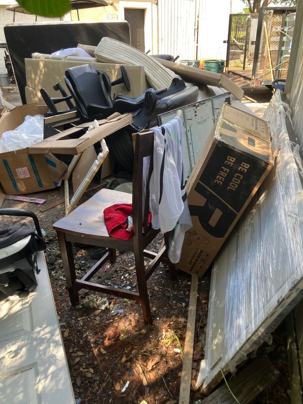 Discarded furniture and boxes piled outdoors in a cluttered space.