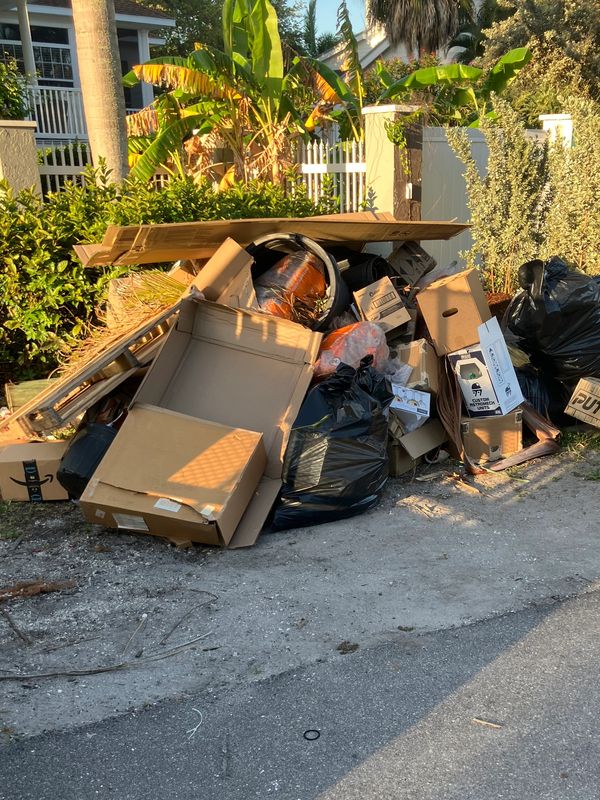 Pile of discarded cardboard boxes and black trash bags on a roadside.