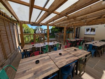 Outdoor seating area with wooden tables and colorful chairs under a wooden pergola.