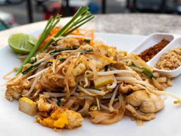 A plate of chicken pad thai with lime and condiments.