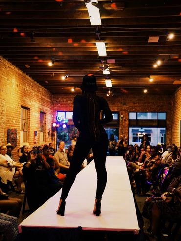 Model walking on runway during indoor fashion show.