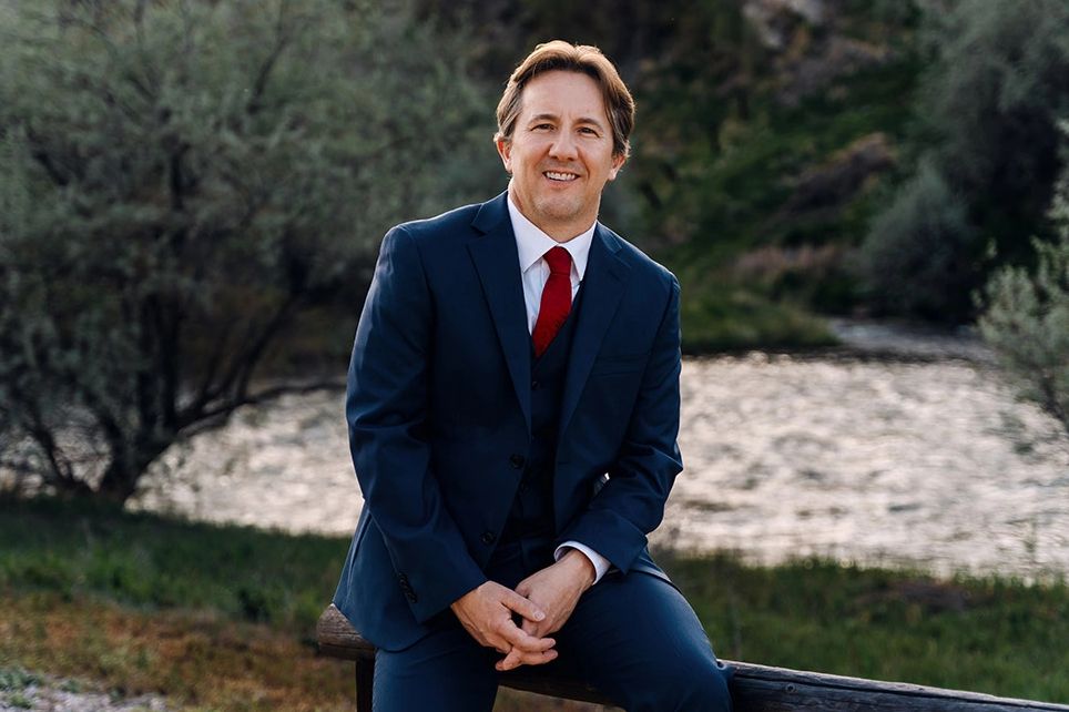 Man in a suit sitting outdoors near water.