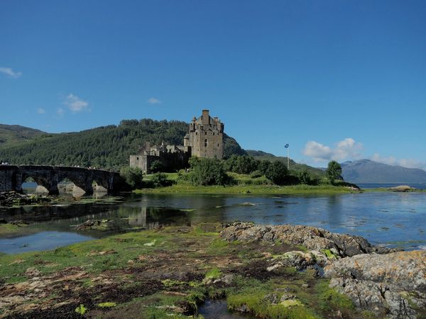 Island castle with stone bridge and clear blue sky.