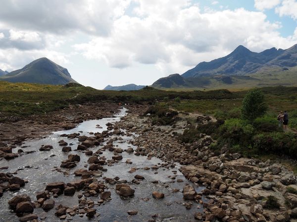 Rocky river flowing through a mountainous landscape under a partly cloudy sky.