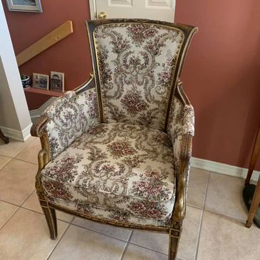 Vintage upholstered armchair with ornate floral fabric and wooden frame.