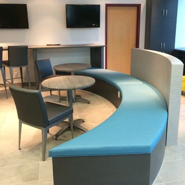 Modern seating area with curved blue bench and round tables in a break room.