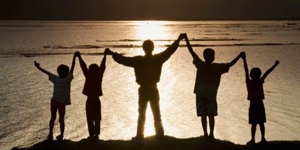 Silhouettes of five people holding hands at sunset by the water.