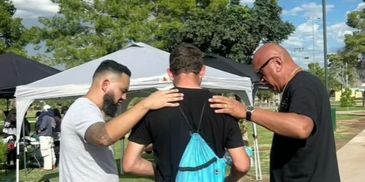 Three men outdoors, two with hands on the shoulders of the third.