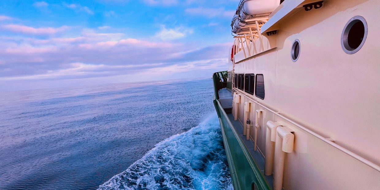 View from a boat sailing on calm blue ocean under a partly cloudy sky.