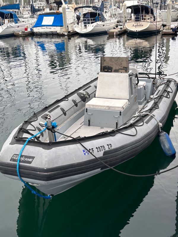 A gray inflatable boat docked in a marina with several sailboats in the background.