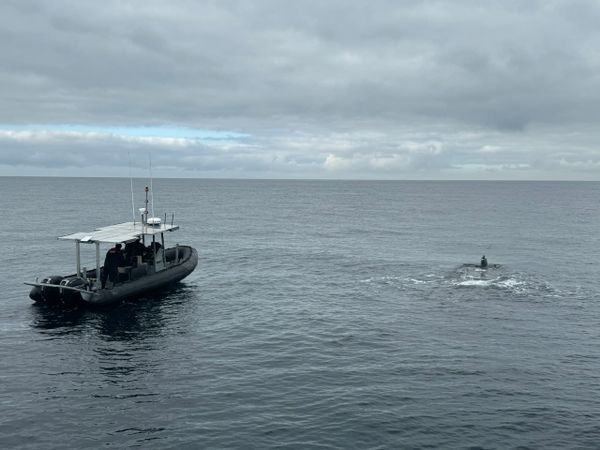 A small boat and a person on a surfboard in calm ocean waters under a cloudy sky.