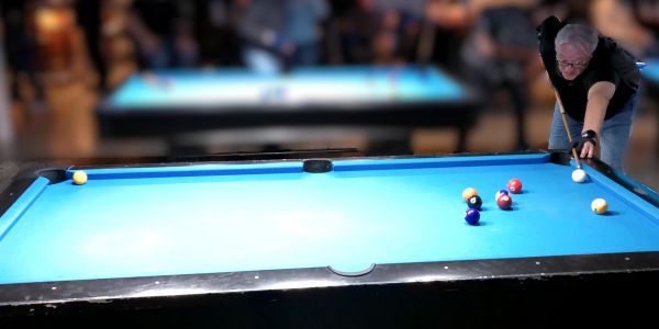 Man aiming to strike billiard balls on a pool table in a dimly lit room.