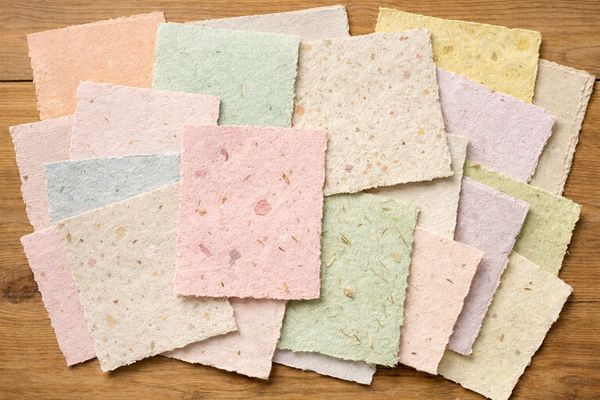 Assorted pastel-colored handmade paper sheets with textured fibers.