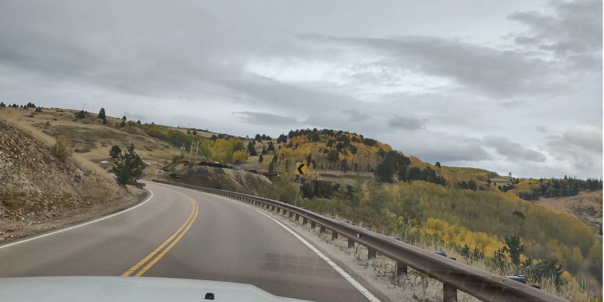 Curvy mountain road with autumn trees under a cloudy sky.