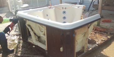 Junk Monkees dismantling a hot tub for removal beside a home.