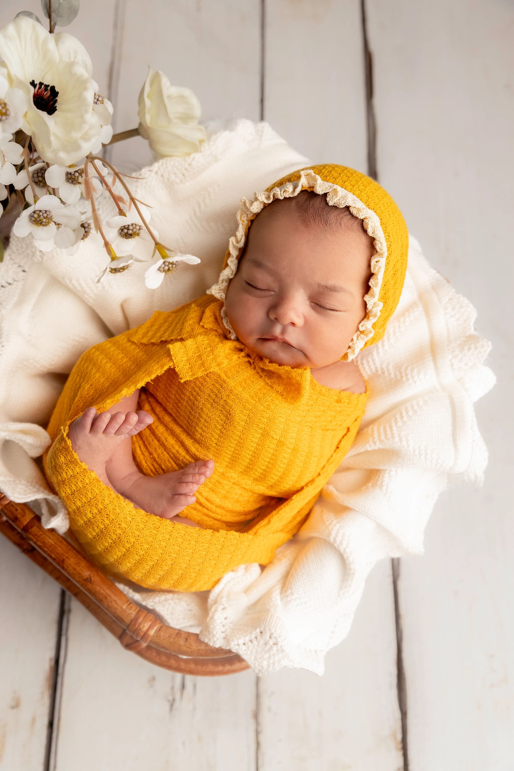 Sleeping baby wrapped in a yellow knit outfit with white flowers nearby.