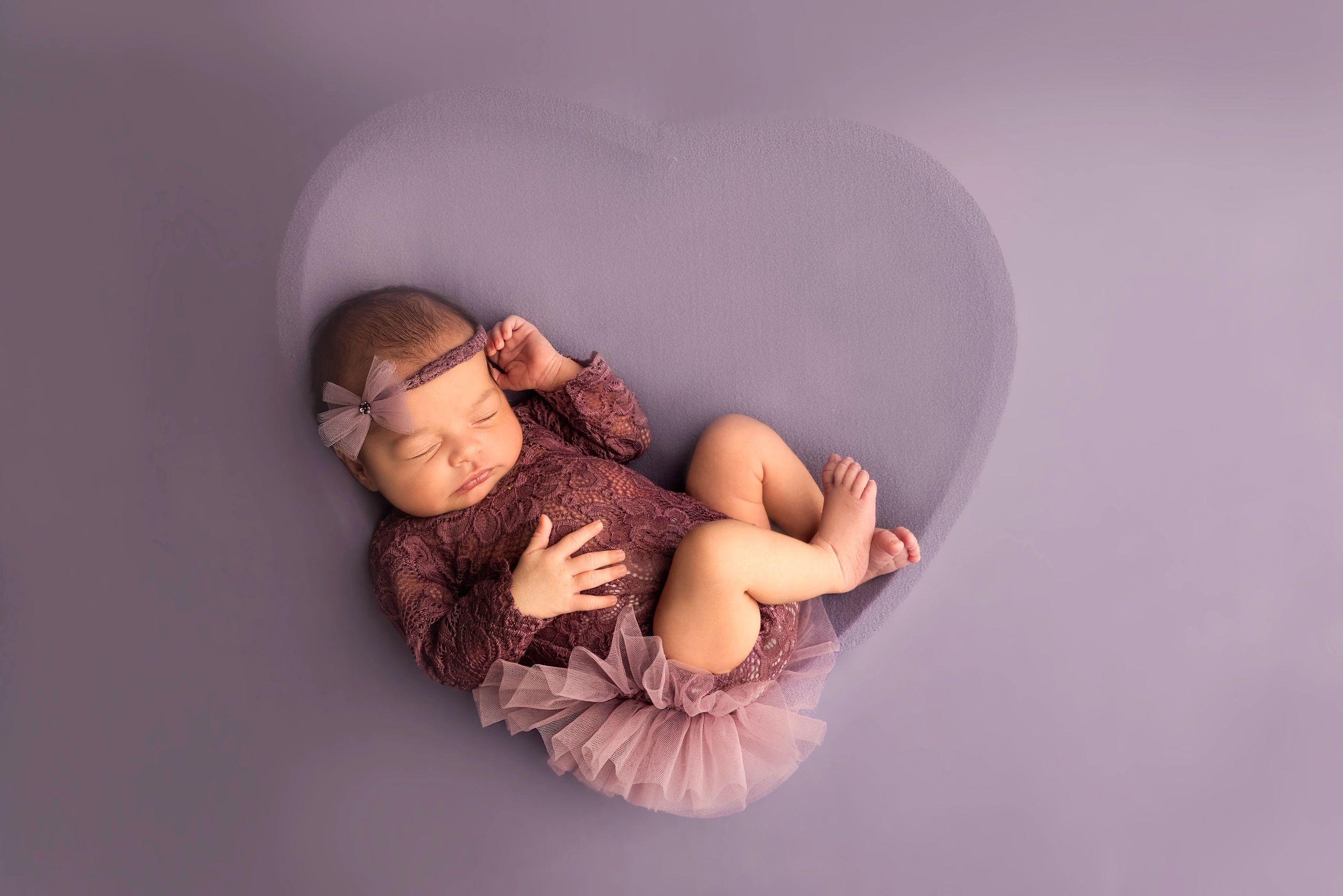 Sleeping baby girl in purple lace outfit on a purple background.