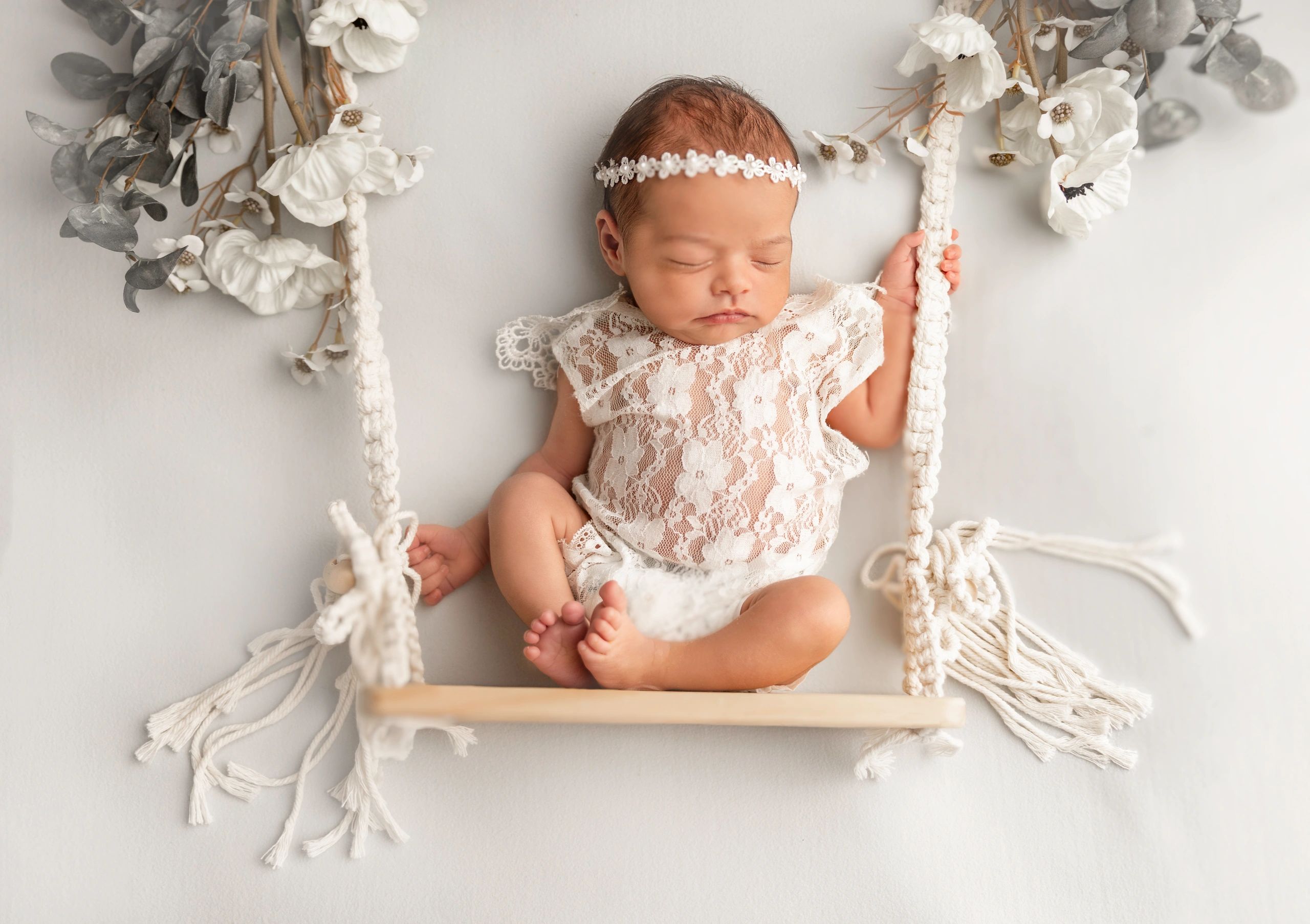 Sleeping newborn baby girl in lace outfit on a floral swing.