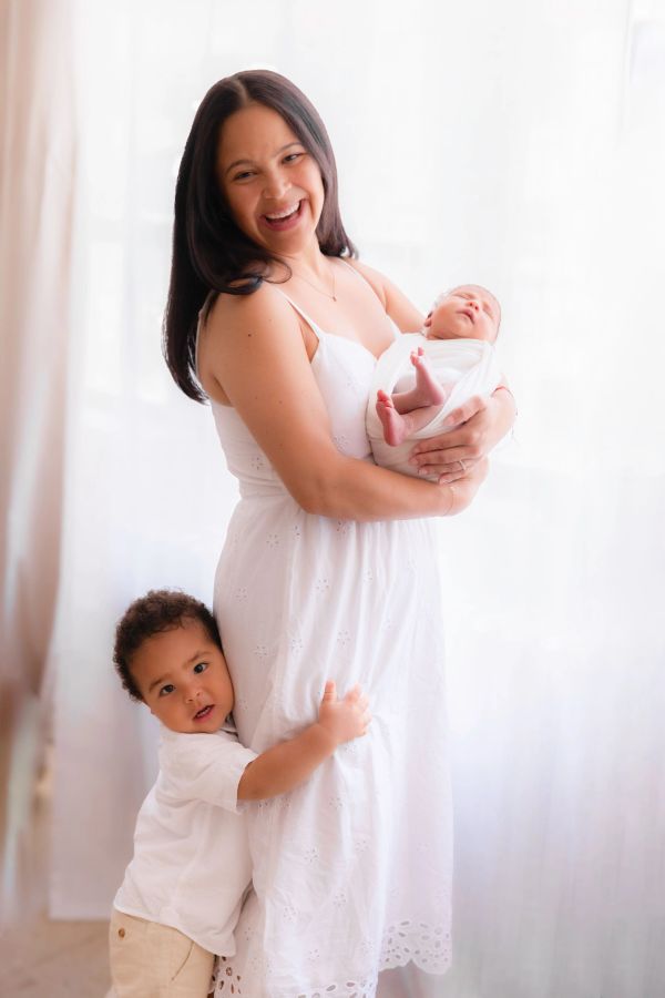 Mother holding newborn with toddler hugging her leg.