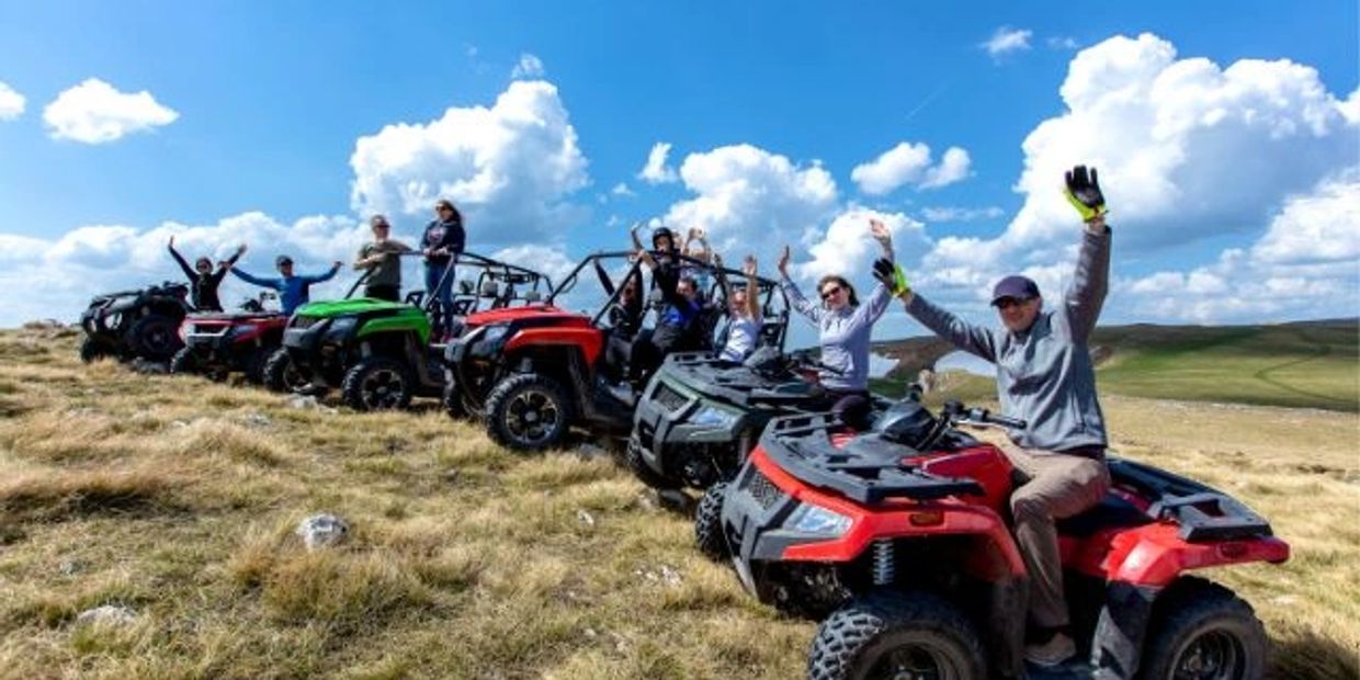 Group of people on ATVs in open grassy field waving.