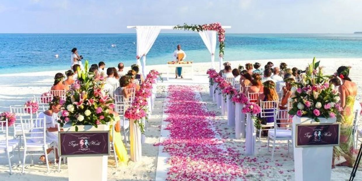 Beach wedding ceremony with floral decorations and ocean backdrop.