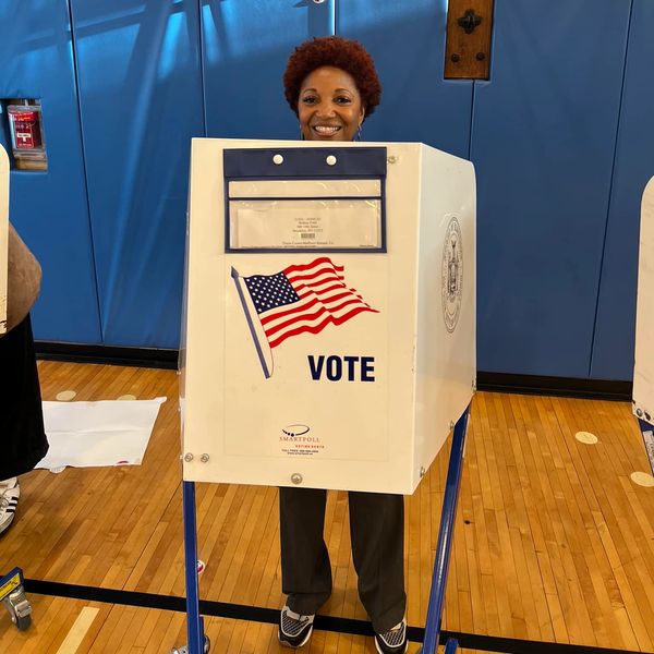 Person smiling behind a voting booth with a US flag.