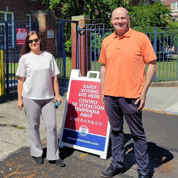 Two people standing beside an early voting site sign outdoors.