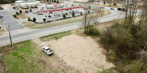 A pickup truck parked on a dirt patch near a road and gas station.