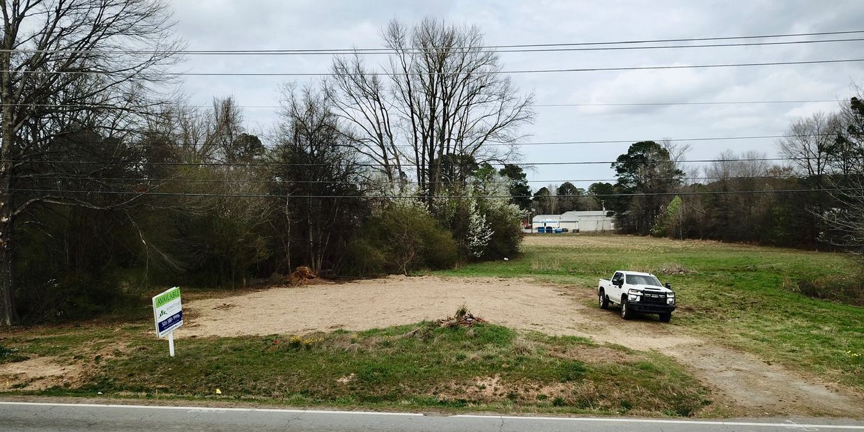 Empty land with a white pickup truck and an 'Available' sign beside a road.