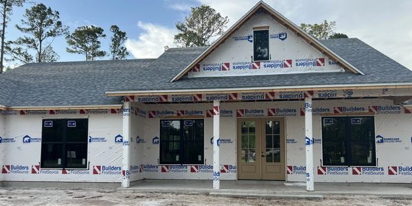 New house under construction with protective wrap and installed windows.