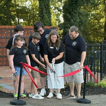 A group cutting a red ribbon at an outdoor event.