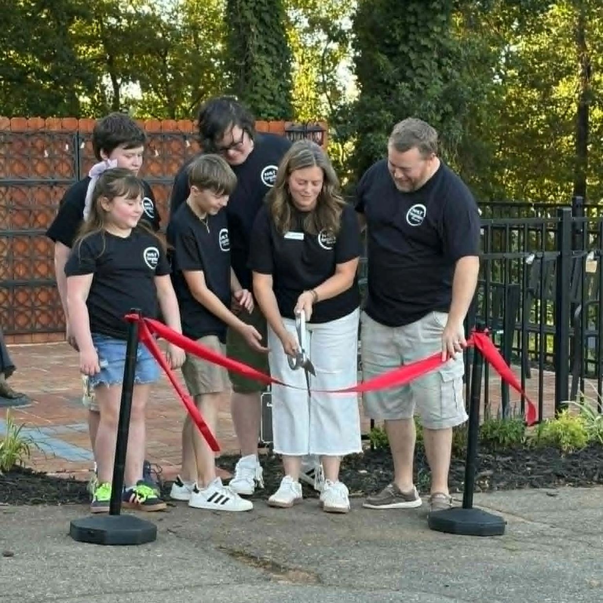 A group cutting a red ribbon at an outdoor event.