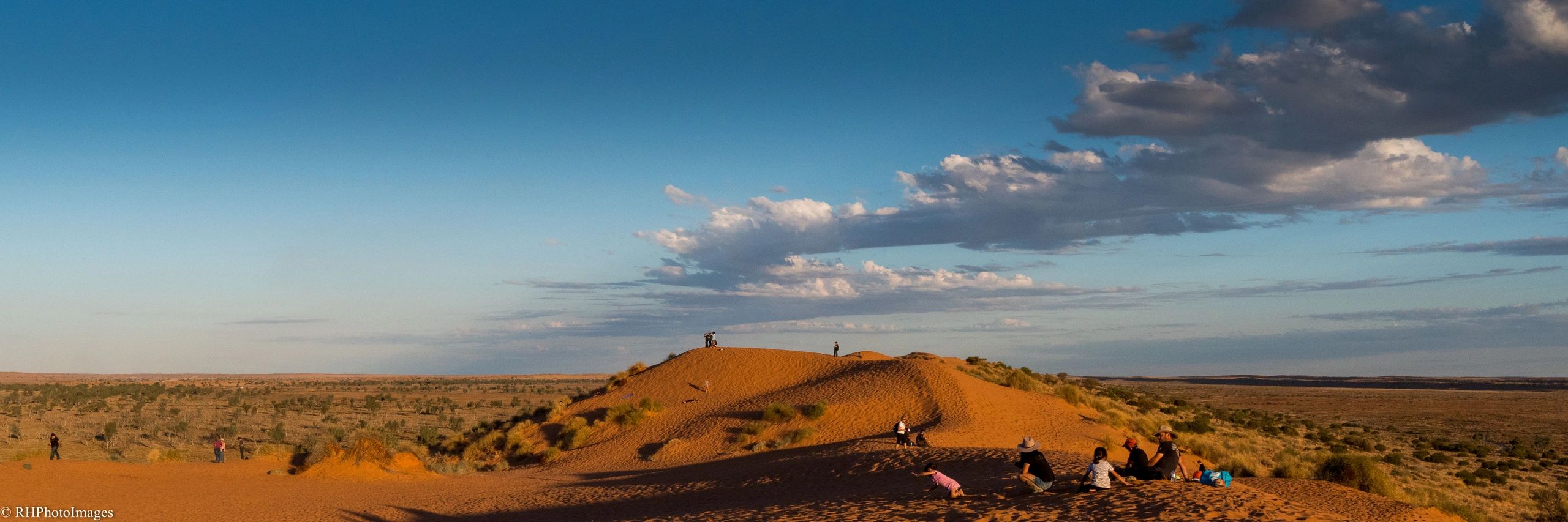 People enjoying a scenic desert landscape with orange sand dunes under a blue sky.